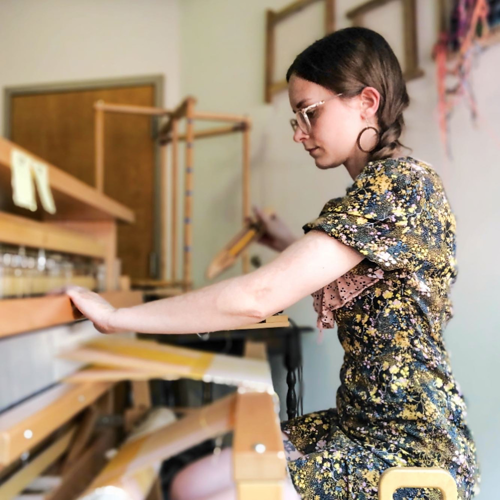 A modern weaver working at a floor loom, ready to throw the shuttle.