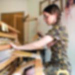 A modern weaver working at a floor loom, ready to throw the shuttle. 