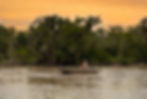 Man fishing from a small boat on the peaceful St. Johns River in Putnam County Florida during golden hour, surrounded by trees draped in Spanish moss