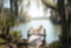 Woman relaxing in a white Adirondack chair on a private dock, holding a cup of coffee and looking out at the calm St. Johns River in Putnam County Florida