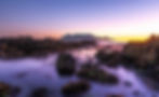Rocky coast sunset photography with purple water and distant mountain