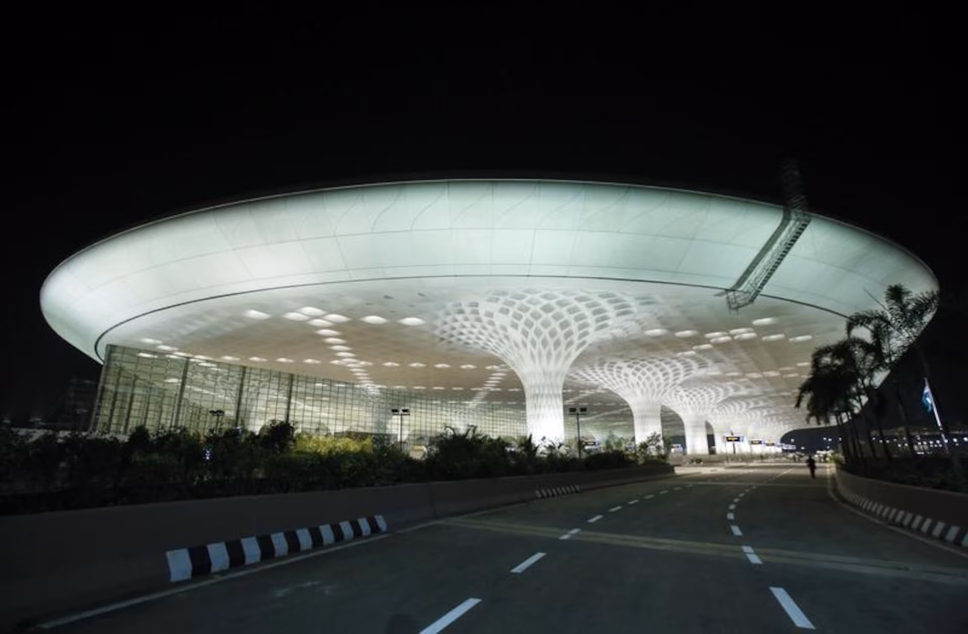 Navi Mumbai International Airport under construction during evening, illuminated terminal building with modern curved architecture.
