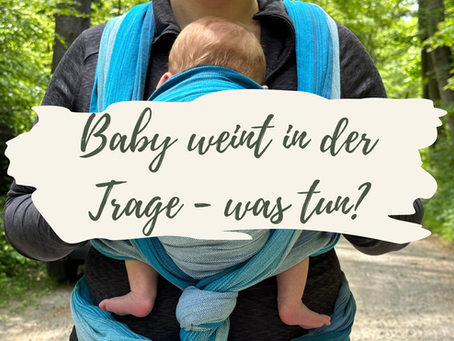 Ein Vater trägt sein Baby in einem blauen Tragetuch und legt liebevoll seine Hände auf Babys Rücken.
