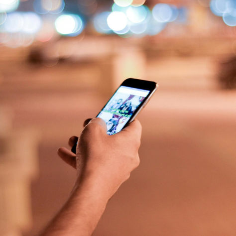 Mano che tiene uno smartphone accesa in modalità automatica durante una camminata serale. Simbolo dell’uso inconsapevole del telefono nella vita quotidiana.