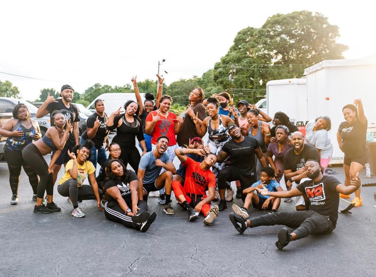 A large JTM group celebrating with arms raised after finishing an outdoor bootcamp