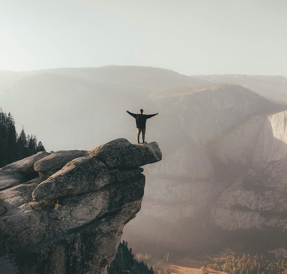 Ein Mann der auf einem Felsen steht, die Arme nach oben reisst und in die weite der Natur blickt.