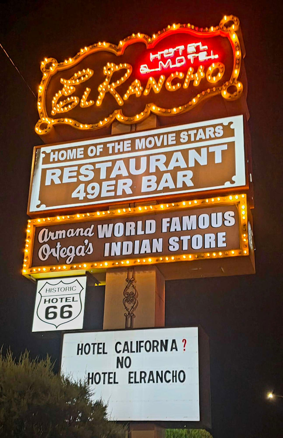 Neon El Rancho Hotel sign on Route 66 at night.