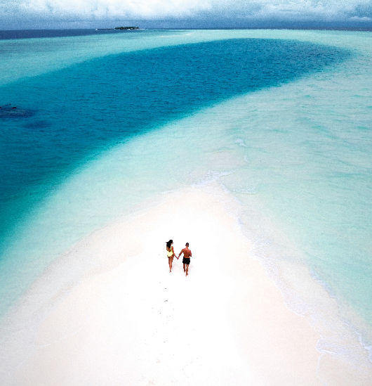Couple walking on white sand beach with turquoise sea