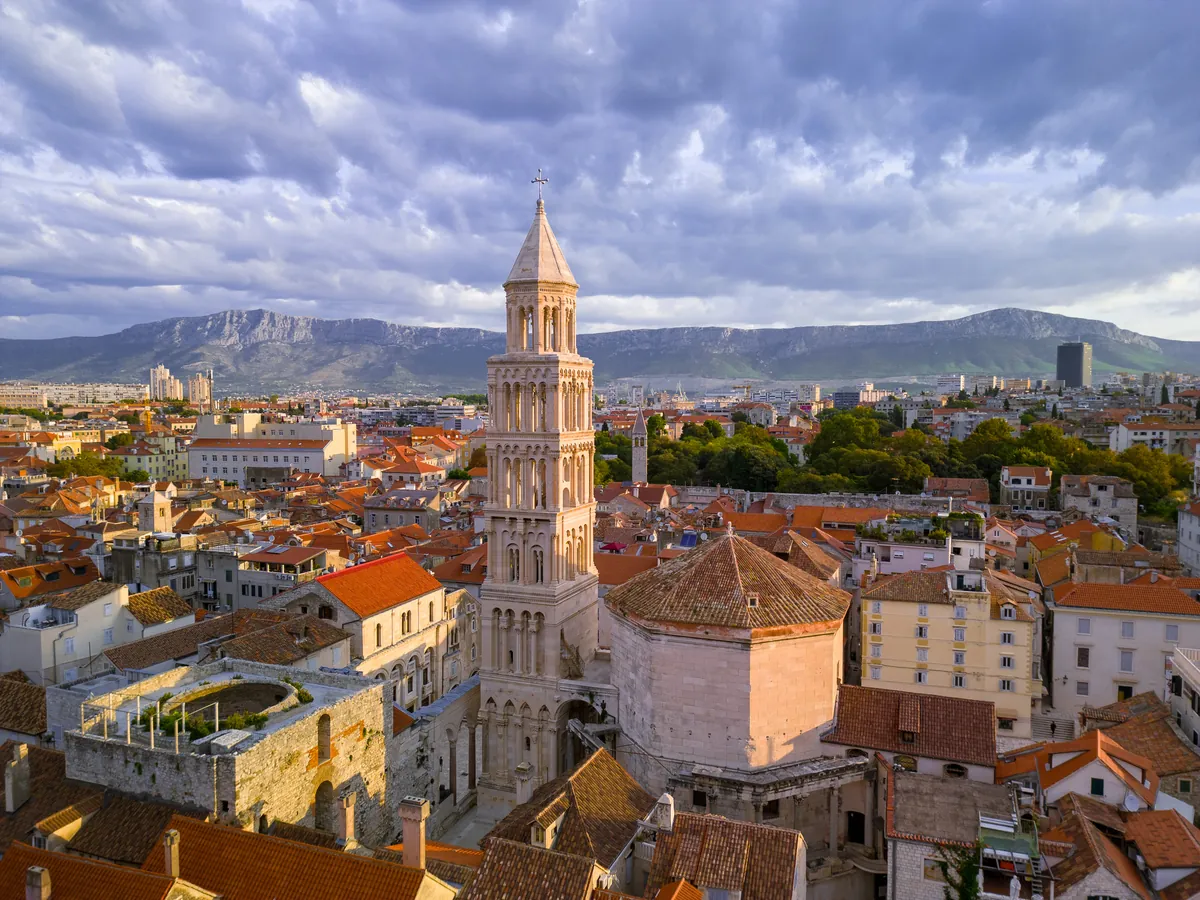 Split rooftops and cathedral bell tower with mountains beyond