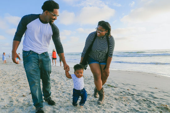 Parents walking hand in hand with toddler on sandy beach_edited