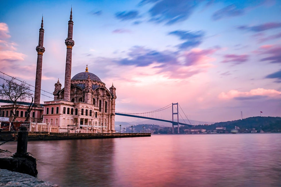 Ortaköy Mosque illuminated at dusk beside the Bosphorus Bridge in Istanbul, Turkey, with city lights reflecting on the water.