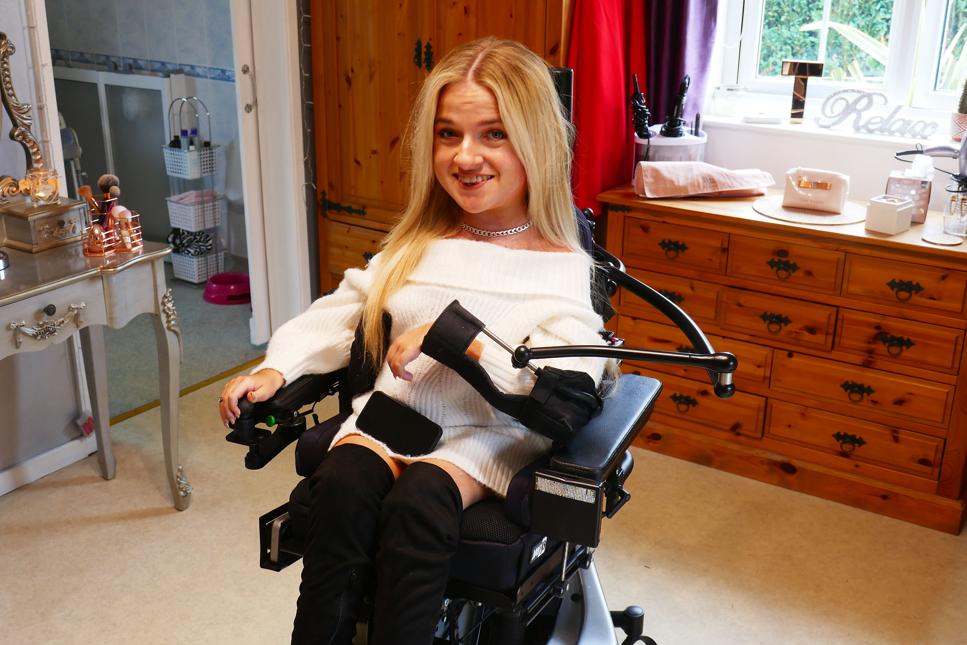 A woman home from university sitting in her bedroom wearing her mobile powered arm supports attached to her wheelchair