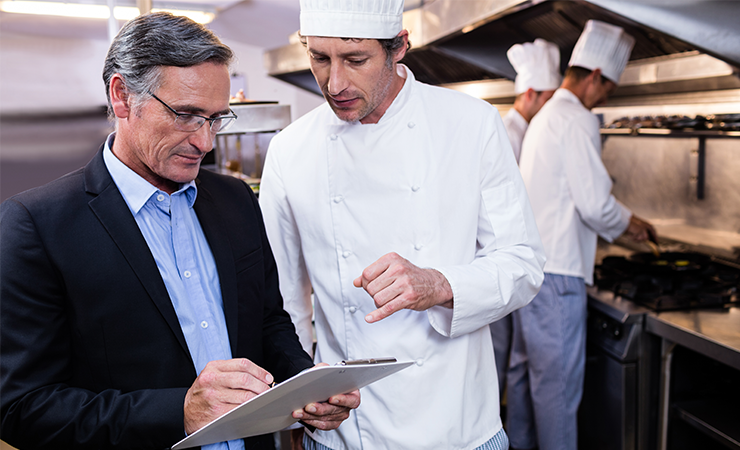 A chef talking to a man who is holding a clipboard.