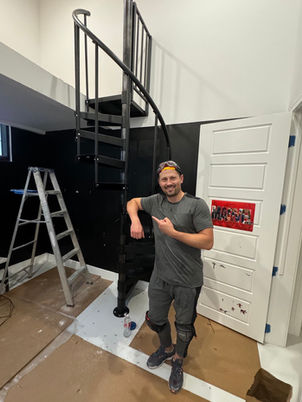 Handyman standing beside newly installed spiral staircase in a modern interior remodel