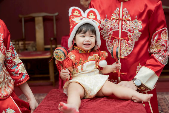 中式抓周過程中寶寶抓取傳統道具，親友在旁陪伴紀錄寶寶的抓周瞬間