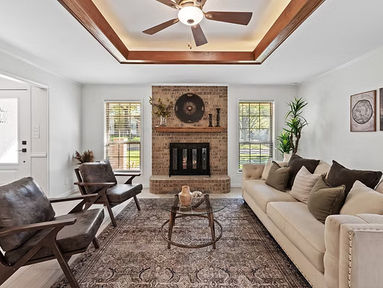 Neutral living room with brick fireplace, beige sofa, wood ceiling detail, and modern chairs