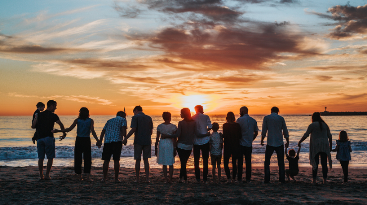group of people gathered on the beach looking out at sunset