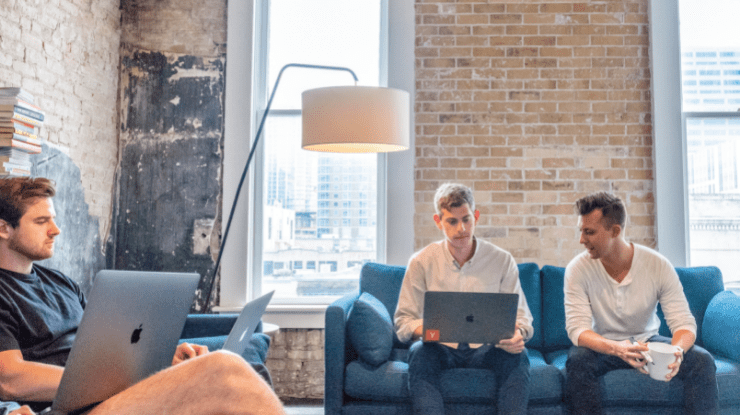 men sat on blue sofas on laptops in co working space