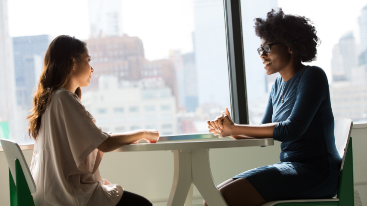 two women sat at a table having a meeting in front of a large window