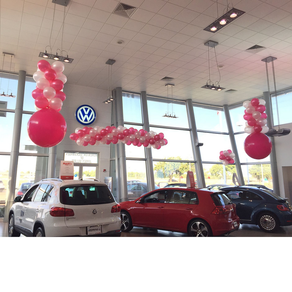 Volkswagen dealership showroom decorated with pink and white balloon garlands and large ba