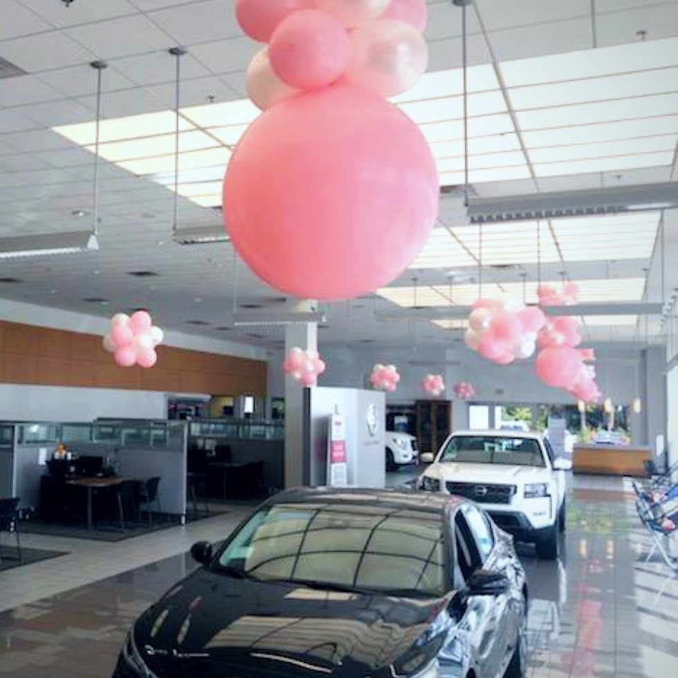 Car dealership showroom decorated with large pink balloon toppers and pink and white ballo