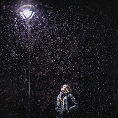 A person in winter clothing looking up at a streetlight in the snow at night