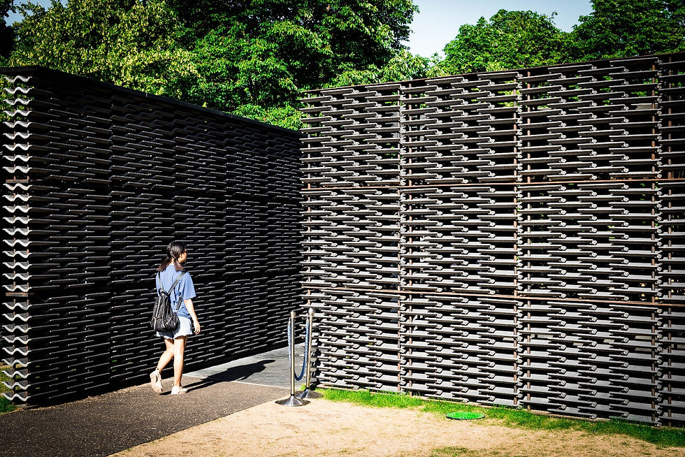 Person walking into 2018 Serpentine pavilion between 2 walls of concrete roof tiles