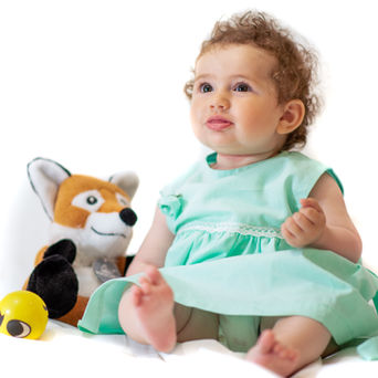 Bambina riccia seduta accanto a una volpe di peluche.