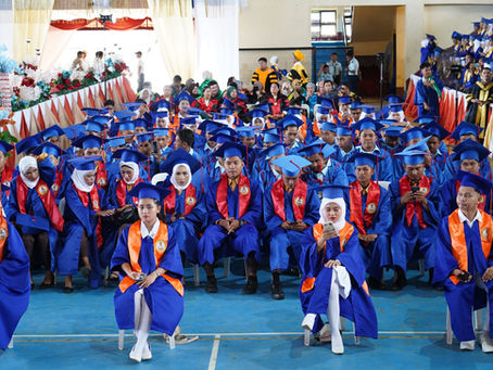 Future nurses in blue, white, and orange caps and gowns at the June 2024 nursing graduation ceremony, standing proudly in a room filled with excitement and accomplishment.
