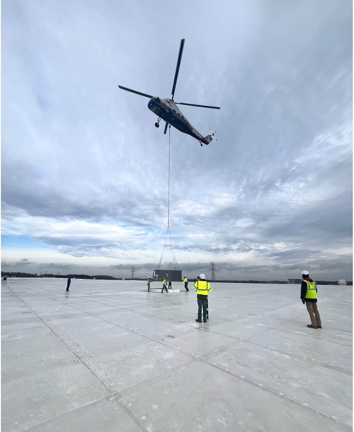 Large HVAC unit being lifted by helicopter onto commercial building