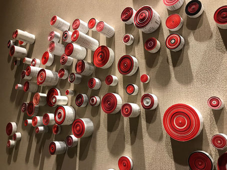 Circular rolls of red and white paper intricately arranged on a textured wall create a captivating art installation, blending geometric patterns with vibrant colors.