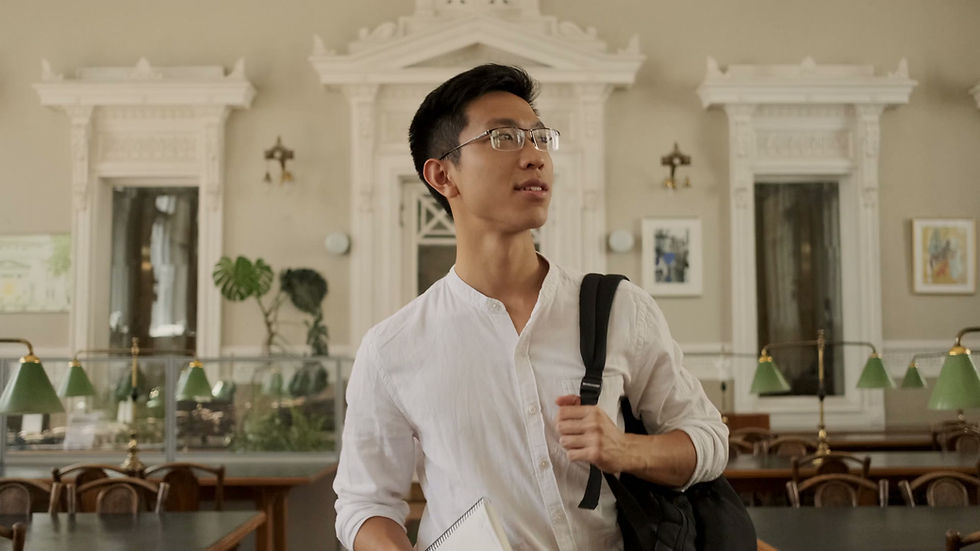Medium shot of young smiling asian male student dreamily walking through library of univer