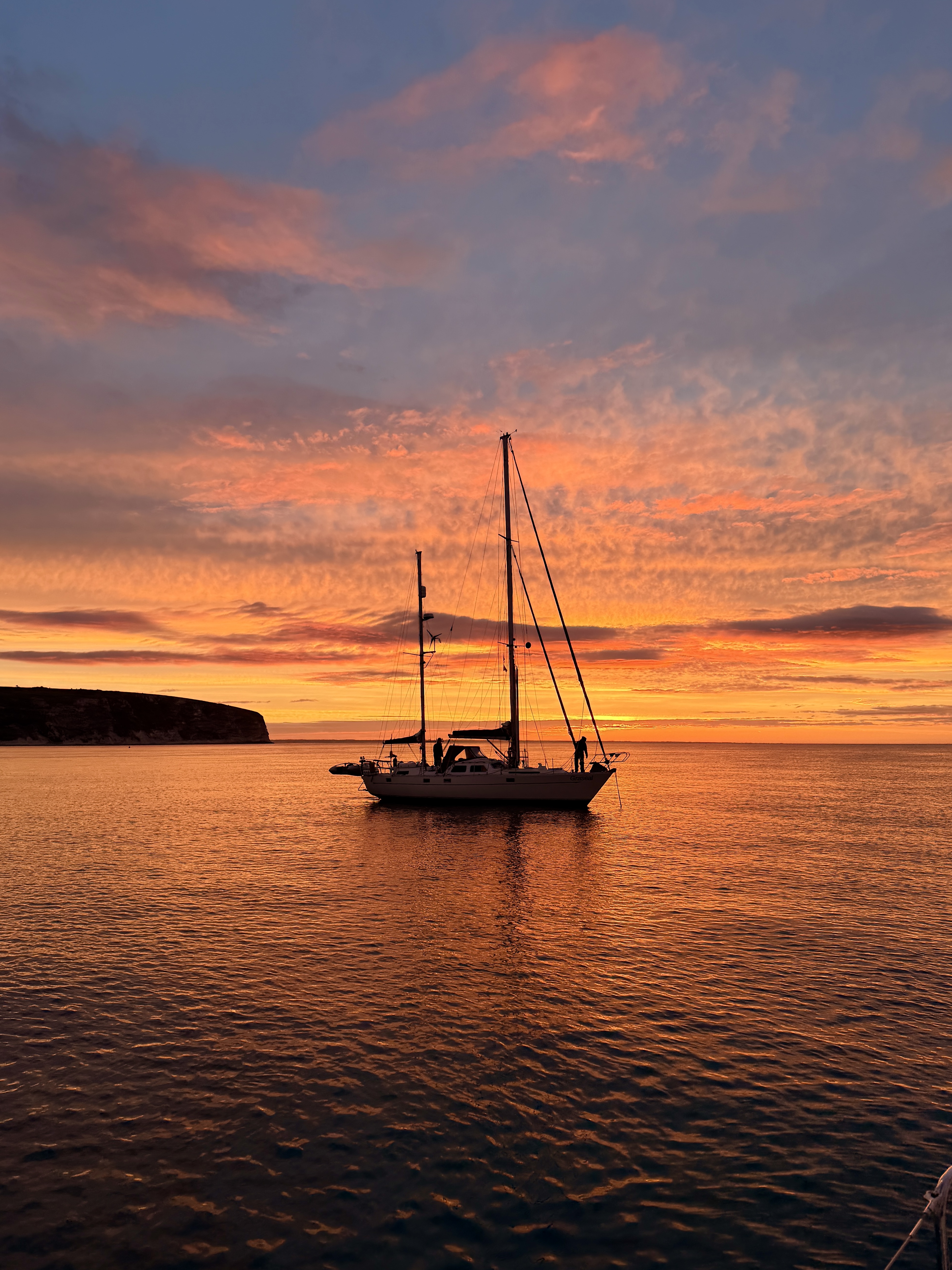 A majestic sailing yacht gliding through the sparkling Solent waters at sunset.