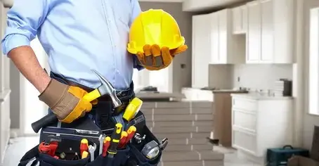 Handyman holding a yellow hard hat and wearing a tool belt in a modern kitchen.