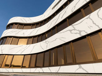 Wide aerial view of a modern commercial headquarters building featuring sweeping curved exterior facade cladding made with MaryFass Calacatta solid surface panels in Turkey.