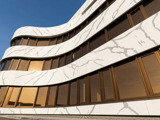 Wide aerial view of a modern commercial headquarters building featuring sweeping curved exterior facade cladding made with MaryFass Calacatta solid surface panels in Turkey.