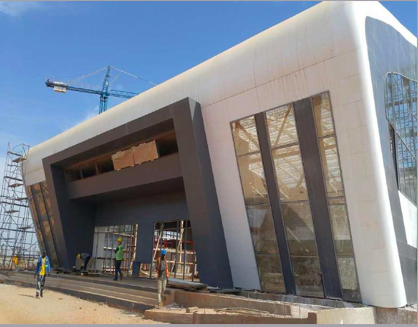 A modern commercial building facade under construction showing a grand curved white structural portal surrounding large window panels.