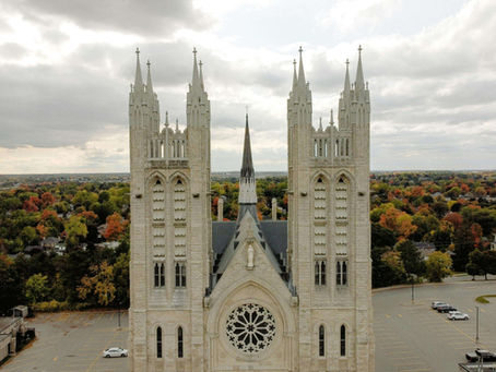 Basilica of Our Lady Immaculate gothic cathedral with twin spires and ornate rose window, set against an autumnal landscape of Guelph with cloudy sky and parking lot below.