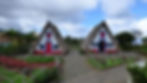 A row of traditional thatched houses in Santana, Madeira, featuring a unique triangular shape and vibrant colors, surrounded by lush greenery.
