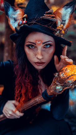 Carmen Hellena in a witch-themed costume: Carmen Hellena dressed in an elaborate witch-themed costume, complete with a hat and mystical accessories, posing in a forest setting with intense and magical expressions.
