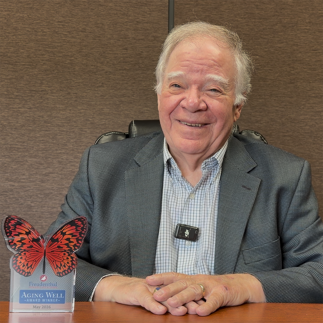 Ken Rosenauer smiles while seated at a conference table with his May 2026 Freudenthal Aging Well Award displayed beside him.