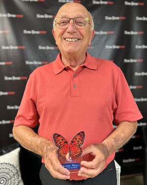 George Szczepanik smiling while holding his Aging Well Award, wearing a coral polo in front of a News-Press NOW backdrop.
