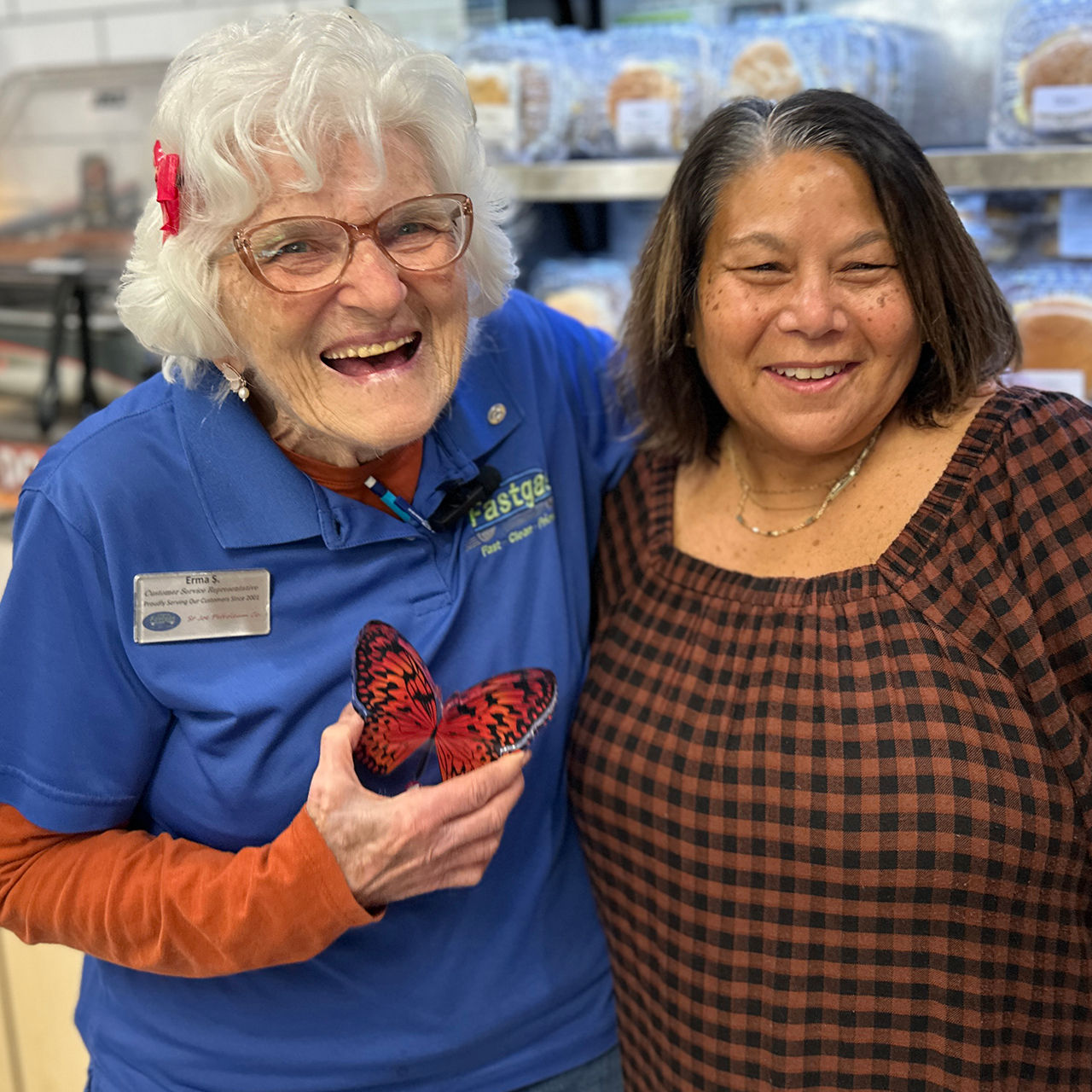 Erma Snodgrass and Bibi from Freudenthal share a joyful laugh together as Erma holds her Aging Well Award. Both women stand in front of a shelf filled with baked goods inside the convenience store.