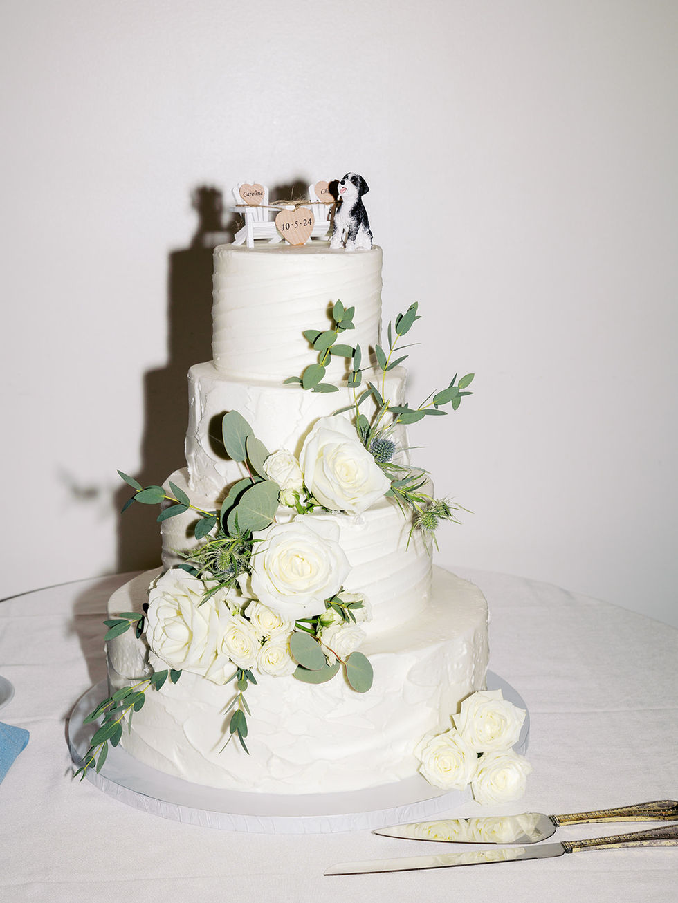 White four-tier wedding cake, roses, green foliage, dog toppers