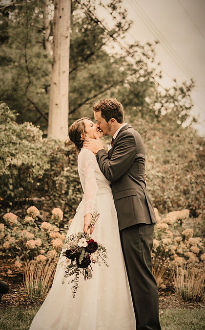 Un couple échange un baiser en pleine nature, sous un décor fleuri de cérémonie.