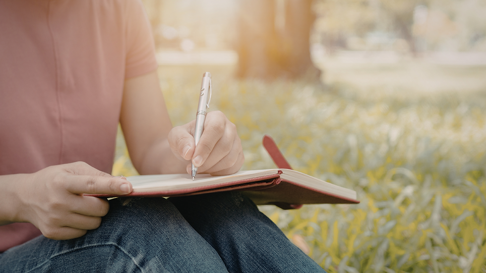 Woman sitting on grass in nature writing in a journal during a calm outdoor moment