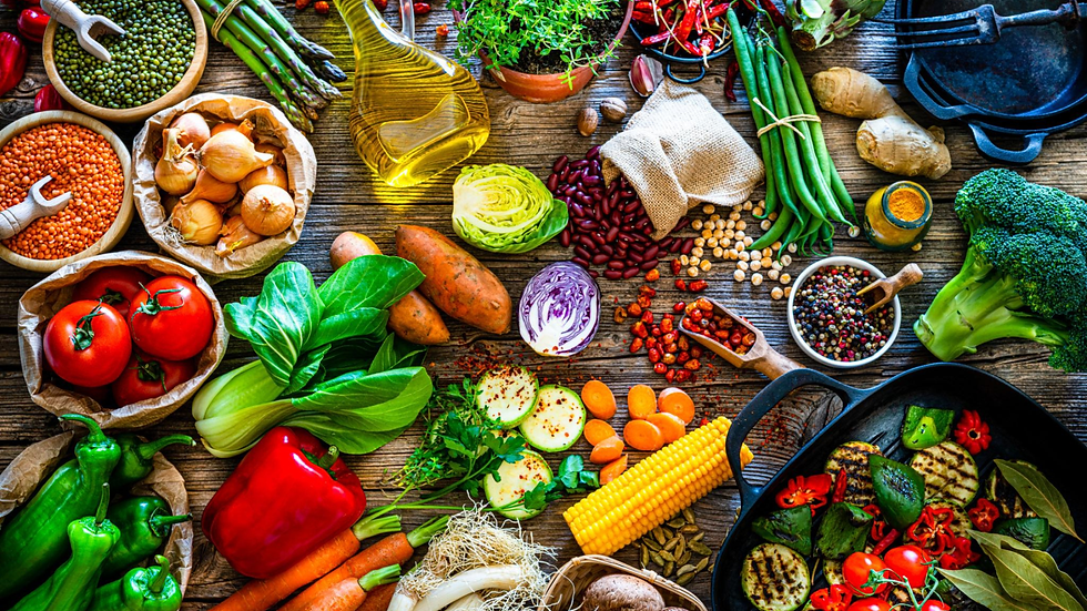 Colorful assortment of fresh vegetables, beans, spices, oil, and cast-iron pans arranged on a rustic wooden table.