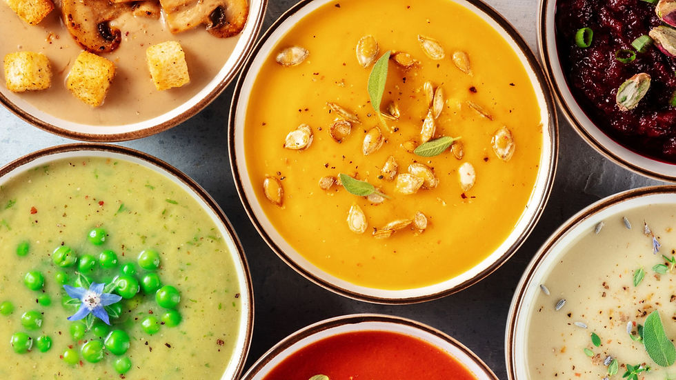 Colorful bowls of soup on a table: mushroom with croutons, pumpkin with seeds, pea with flower, and beet with seeds. Vibrant and appetizing.