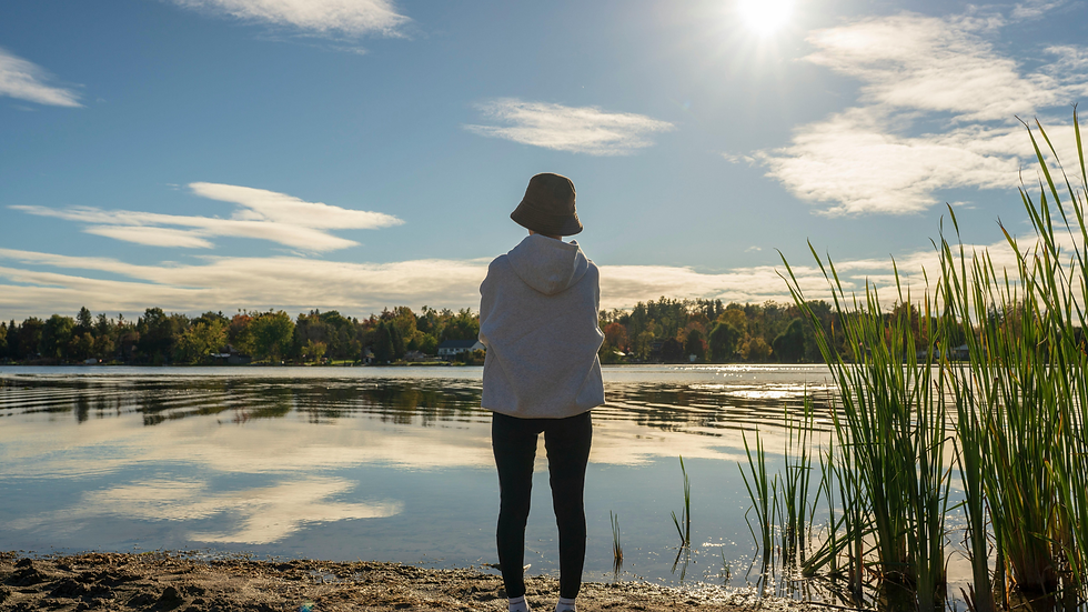 Woman sitting peacefully on a dock by a lake in natural sunlight, reflecting mindfulness, inner calm, and holistic Ayurvedic wellness for body, mind, and spirit