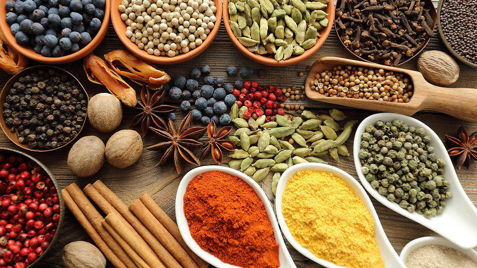 Assorted whole and ground spices in bowls and spoons on a wooden table, including peppercorns, cardamom, cinnamon, and star anise